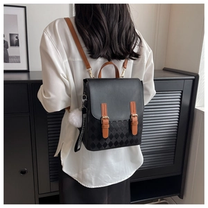 Detail eines schwarzen gesteppten Rucksacks mit braunen Gurten und Plüschball-Anhänger