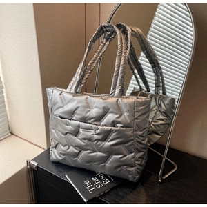 Detailed view of silver puffer tote bag with quilted texture and fashion logo label