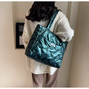 Close-up of a large green quilted tote bag with metallic glossy finish and white fashion label