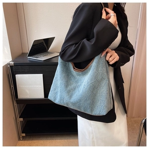 Close-up of light blue denim tote bag with brown leather trim and diamond quilted stitching