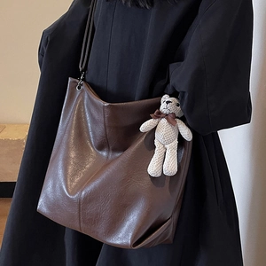 Large brown leather tote bag with a small bear pendant on a model in a black coat