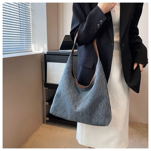 Detail of blue denim tote bag with brown leather straps shown in a modern interior setting