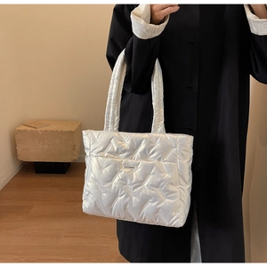 Silver quilted tote bag featured on a model in a black coat showing large capacity