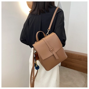 Dettaglio posteriore di uno zaino vintage in pelle marrone con ciondolo su una modella