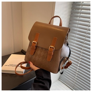 Detail eines karamellbraunen Lederrucksacks mit Steppmuster und Plüschball-Anhänger