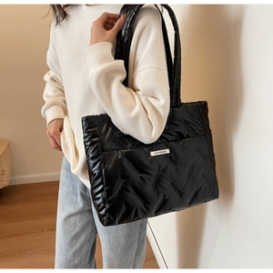 Detail of black quilted tote bag showing padded texture and white fashion label on shoulder
