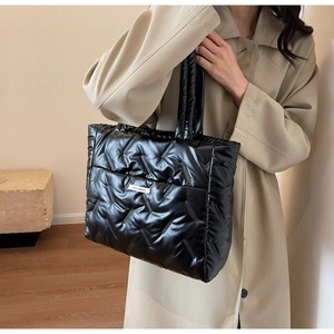 Detail of black glossy quilted tote bag with a brand label on a soft nylon texture