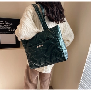 Detail of dark green quilted tote bag with metallic finish shown on a shoulder