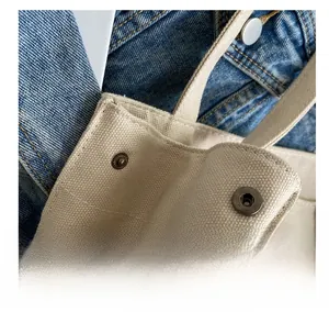 Detail of vintage metal snap button closure on a cream canvas tote bag with denim background