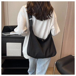 Vue arrière du modèle portant un grand sac bandoulière en nylon noir avec sangle