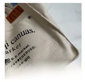Close-up of cream canvas tote bag showing precise stitching, metal rivets and pocket detail