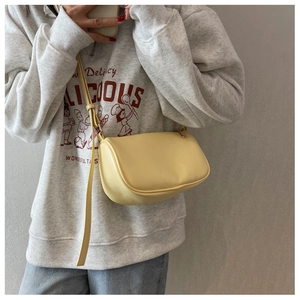 Detail view of light yellow matte leather crossbody pillow bag worn by a model