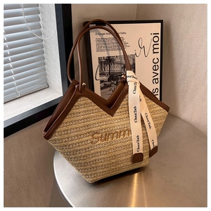Détail du sac cabas en paille avec anses en cuir marron et broderie Summer sur table