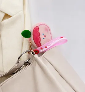 Dettaglio del ciondolo in peluche pesca rosa con cinturino in silicone su borsa crema
