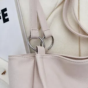 Dettaglio dell'anello in metallo argento e cuciture fini sulla tracolla della borsa beige