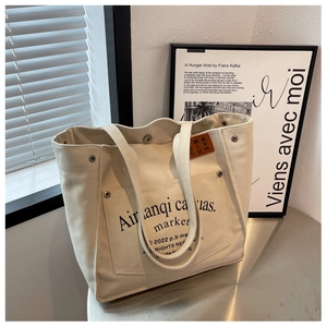 Detail of cream canvas tote with silver button, leather logo, and vintage letter print