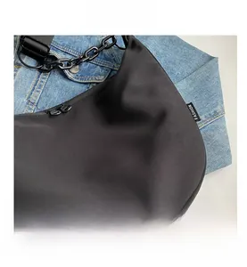 Detail of black crescent canvas crossbody bag with plastic chain on denim background