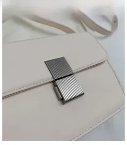 Close-up of textured gunmetal lock on a minimalist beige leather crossbody bag detail