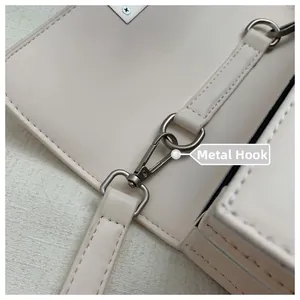 Detailed close-up of matte dark metal clasp and stitching on off-white crossbody bag