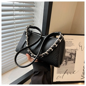 Detalle de bolso negro en piel grabada de cocodrilo con cadena plateada y cremallera