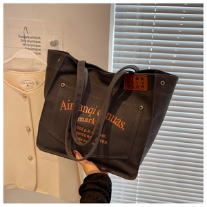 Detail of black canvas tote bag featuring orange letter patches and wide shoulder straps