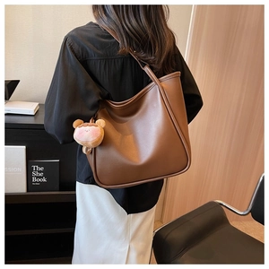 Brown large capacity tote bag with plush charm shown from a back side view on shoulder