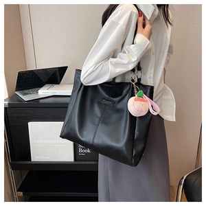 Dettaglio della borsa tote in pelle nera con anelli in metallo e ciondolo a pesca rosa