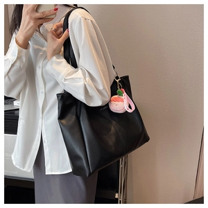 Dettaglio di una grande borsa tote nera in pelle PU opaca con ciondolo a pesca in peluche