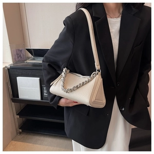 Close-up of cream textured leather triangle bag with silver chain on model in black blazer