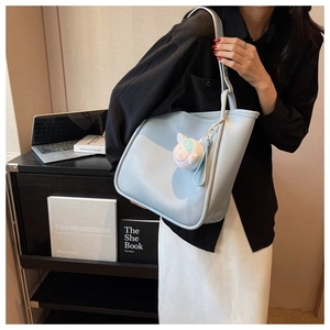 Detail of light blue tote bag with plush ball charm shown in an urban office setting