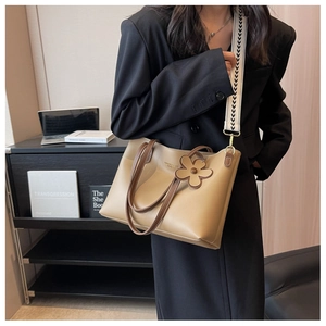 Detail of khaki tote bag featuring wide arrow strap and flower charm on female model