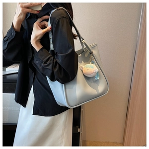 Light blue leather tote bag with plush sheep charm shown from a side profile view