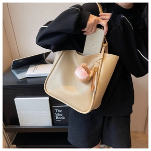 Close-up of beige leather tote bag with plush charm showing spacious interior storage