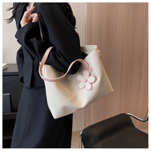 Detail view of large cream tote bag with pink handles and floral charm on model