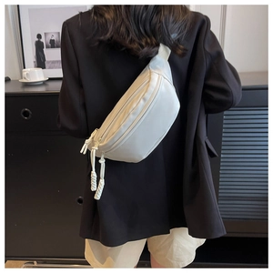 Detail view of cream canvas crossbody chest bag with long woven zipper pull strap