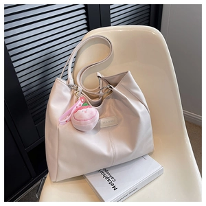 Dettaglio di una grande borsa tote color crema con un ciondolo di peluche rosa