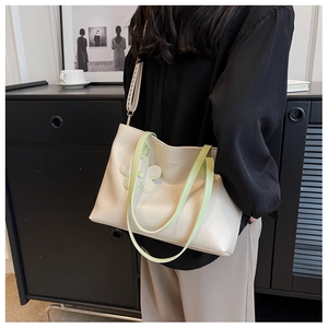 Detail of a large cream tote bag with light green straps and a floral charm on model