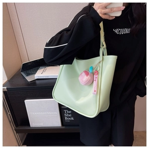 Detail of mint green PU leather tote bag with sweet peach plush charm and shoulder strap