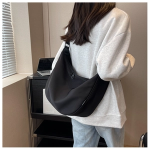 Detail of the large black nylon crescent crossbody bag worn by a model in a casual setting