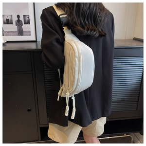 Close-up of minimalist cream chest bag featuring woven zipper pulls on durable nylon fabric