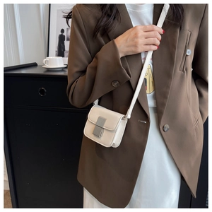 Detail of a creamy white mini crossbody bag with a silver metal clasp on a brown blazer