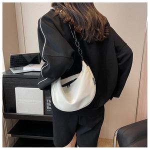 Close-up of a white hobo bag with a chunky black chain strap worn by a model
