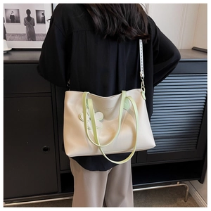 Detail of off-white tote bag with green strap and floral charm on a black shirt model