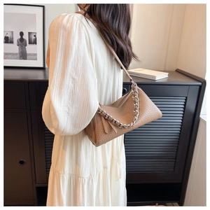 Detalle del bolso acolchado de cuero marrón con cadena plateada y vestido blanco