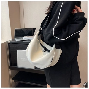 Detail of a white crescent hobo bag featuring a black adjustable strap and metal zipper