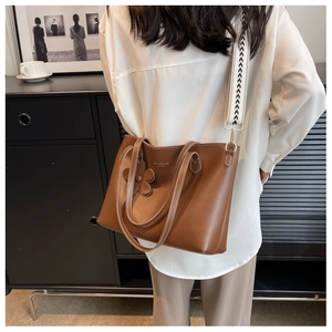 Brown leather tote bag featuring geometric wide strap and flower charm detail
