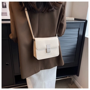 Model wearing cream white minimalist flap bag with rectangular metal clasp and long strap
