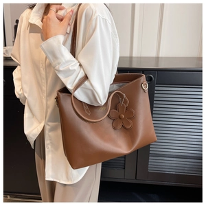 Detail of a brown leather tote bag with white stitching and flower charm pendant