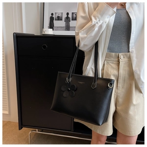 Detailed shot of a black tote bag with white stitching and floral charm accessory