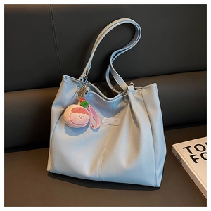 Dettaglio borsa tote azzurra con trama litchi, toppa del marchio e ciondolo rosa